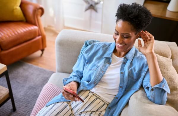 A woman sitting on a couch smiles while looking at her phone