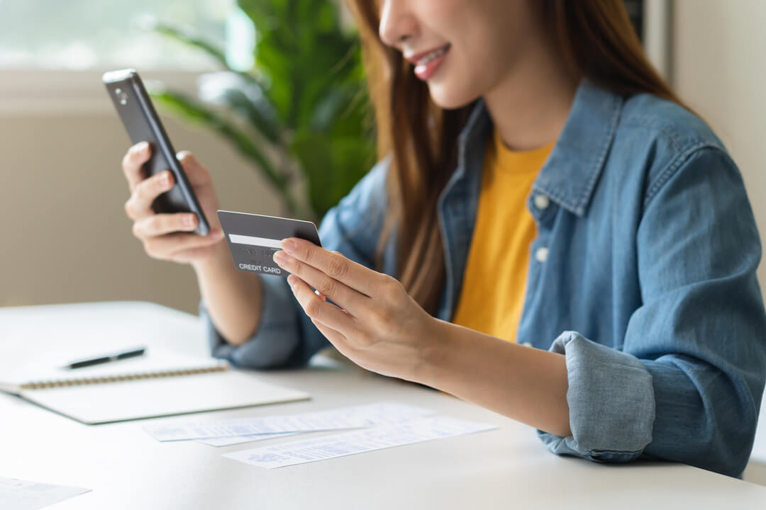 Young woman typing credit card information into smartphone