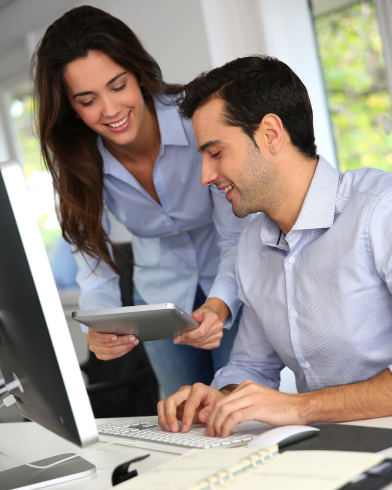 Business man and woman in the office using desktop and tablet internet