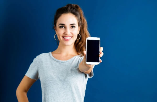Woman holds up her phone to the camera standing against a blue background