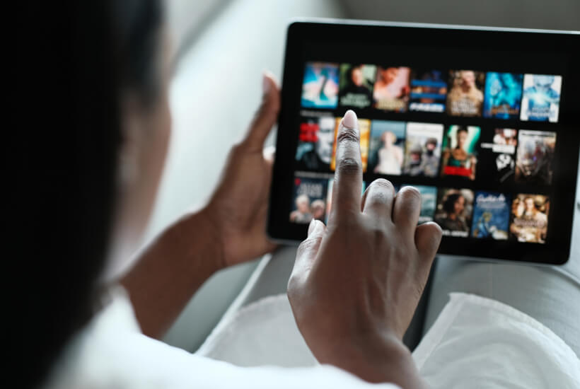 Tablet device with movies populating the screen and a woman's hand about to click one
